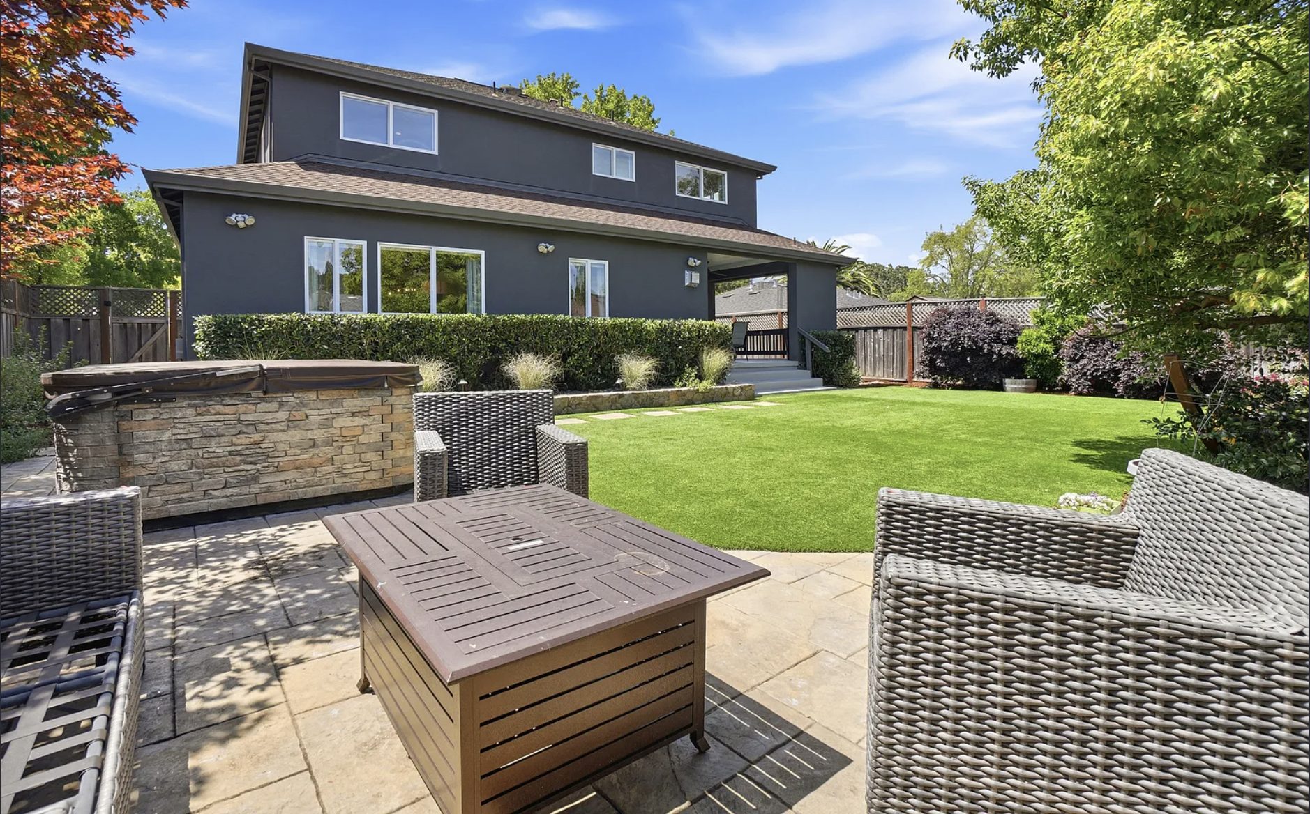 Flat, fully fenced backyard with an artificial-turf lawn, hot tub, and stone patio at a San Rafael home